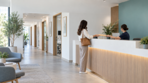Recepción de una clínica privada con una paciente de pie entregando un sobre a la recepcionista